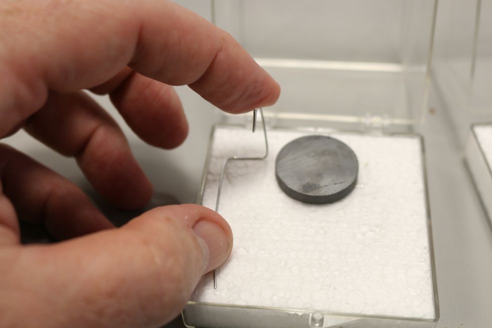 Now take one of your bent wires and place it along one side of the magnet, center the hook so it follows an imaginary line through the center of the magnet. We want the hooks centered so the coil is.