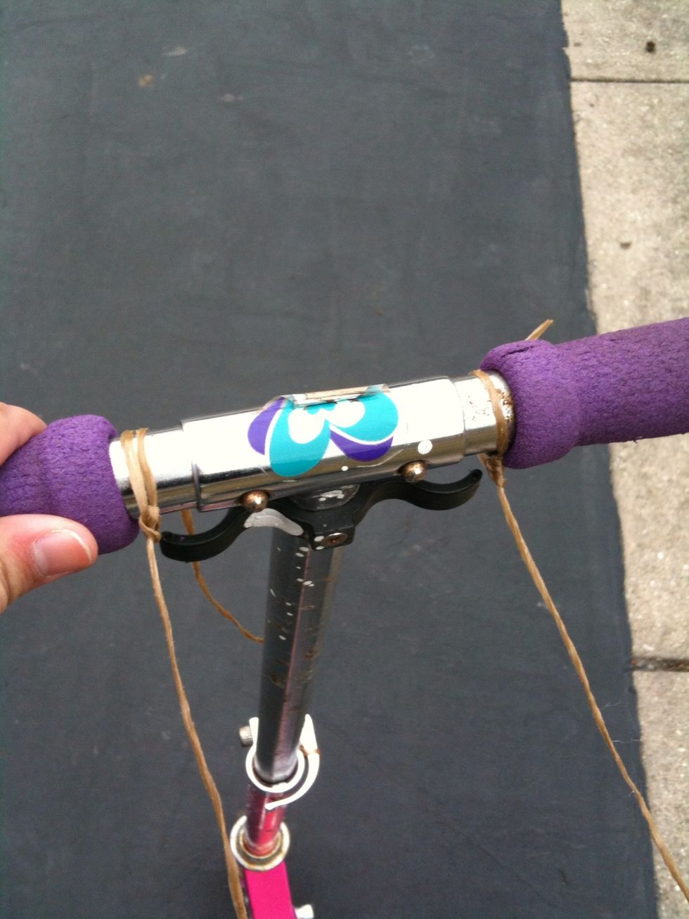 Now take some more twine and divide it into two long pieces, about 3 feet long each. Tie one end of each length to the handles of the scooter, like this.