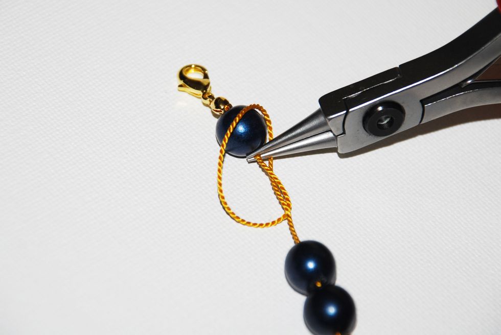 Now that you have a loop, grab the thread inside the loop with the tip of your round nose pliers. Grab the thread as close to the stone as you can.