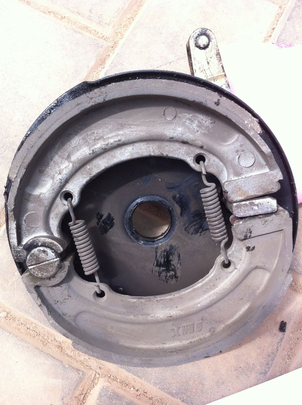 Now the brake assembly will pop out. Inspect and decide for replacement or cleanup. Remove the brake shoes by bending them inwards like the opposite way of breaking bread. Take care of the springs.