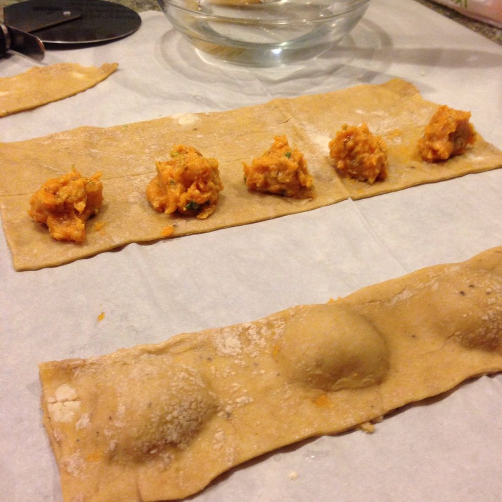 Now the fun begins...carefully fold the blank pasta over the pasta with the dollops of filling. Pinch the edges, and in-between the mounds to indicate the perimeter of the ravioli.