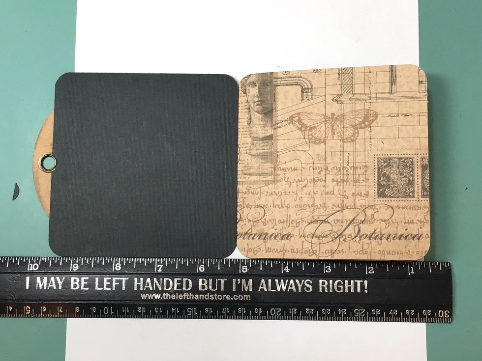 Now we'll attach the front tag, Celebrate, to the pages. Place the back side of the tag firmly against the stitched pages. Use a rule to line up the tag evenly with the pages at the bottom.
