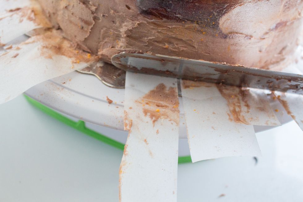 Now we remove the parchment paper strips. I used a cake spatula to stabilize the bottom edge of the cake to prevent icing on the bottom from pulling when you pull away the strips.