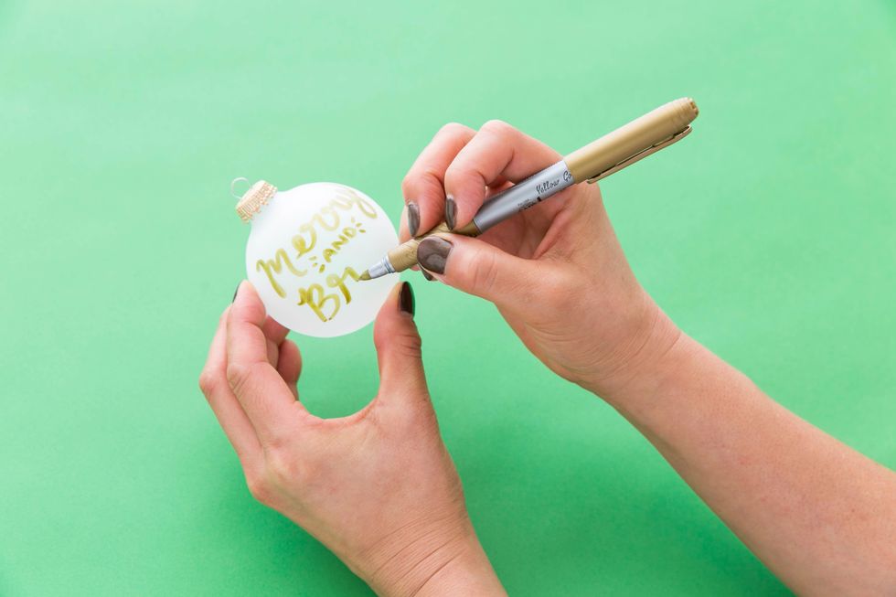 Now, write the holiday saying onto an ornament. Sometimes the metallic pens are too thick to make the second, fauxligraphy line, so you can free hand the thicker strokes.