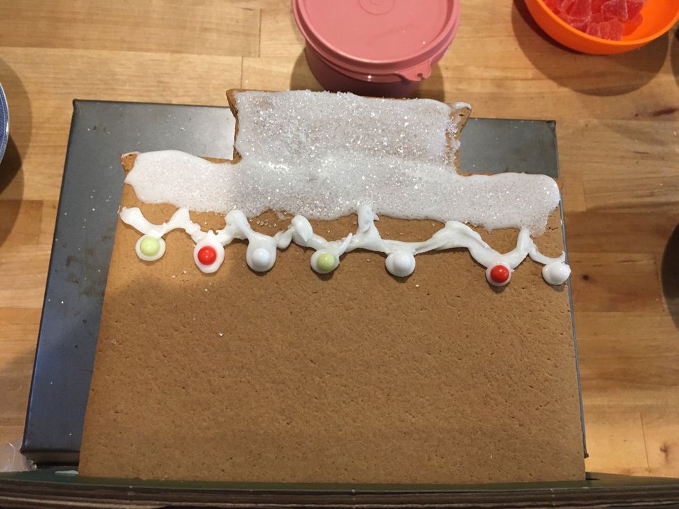 Now you use your watery frosting to spread across the top. Sprinkle the sugar on top as snow. Add Christmas lights with the bead candies