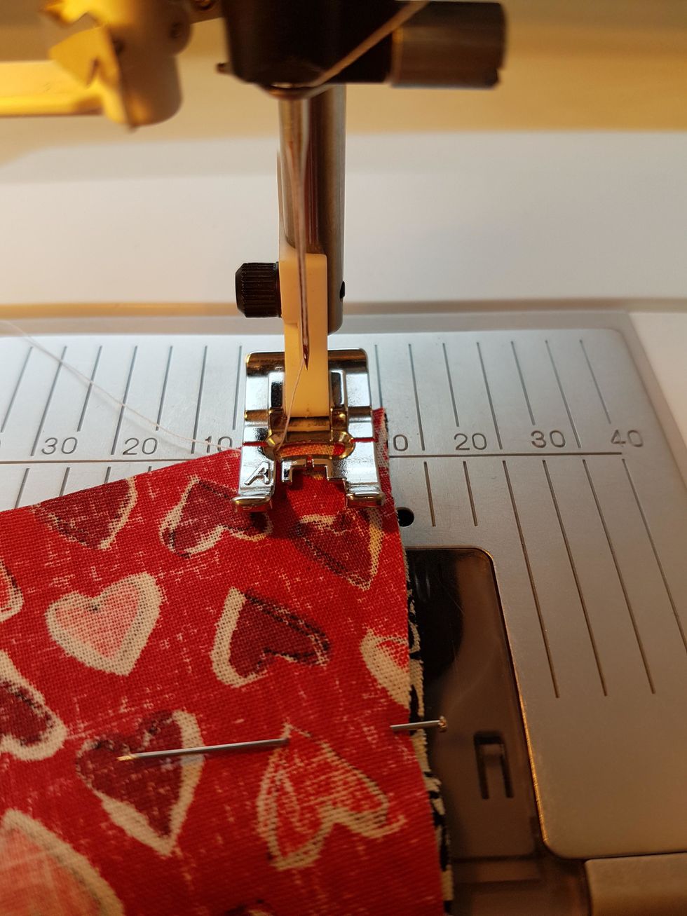 Nu ska du sy ihop de tv\u00e5 l\u00e5ngsidorna. L\u00e4gg arbetet i symaskinen, du ska sy med 1 cm s\u00f6msm\u00e5n. (tyget ska f\u00f6lja 10 strecket till h\u00f6ger om pressarfoten) B\u00f6rja med att sy 5 stygn fram\u00e5t.