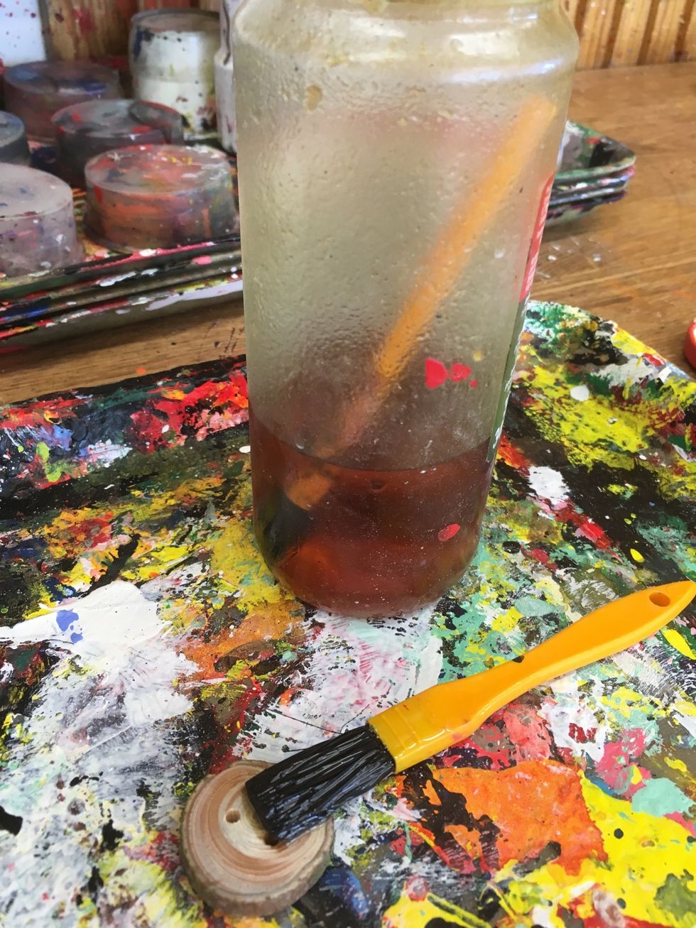 Nu ska du ytbehandla knappen. Ta fram en glasburk med gul/brun olja. L\u00e4gg lite olja p\u00e5 knappen med penseln som \u00e4r i oljan. Endast den penseln f\u00e5r anv\u00e4ndas. Arbeta p\u00e5 en tr\u00e4b\u00e4nk eller bricka.