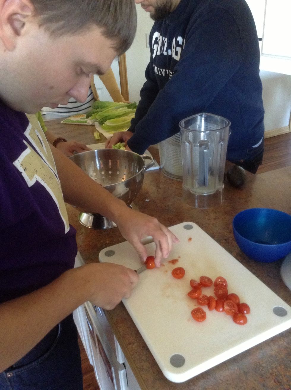 On a cutting board using the knife cute the tomatoes in half. Set aside in a bowl.