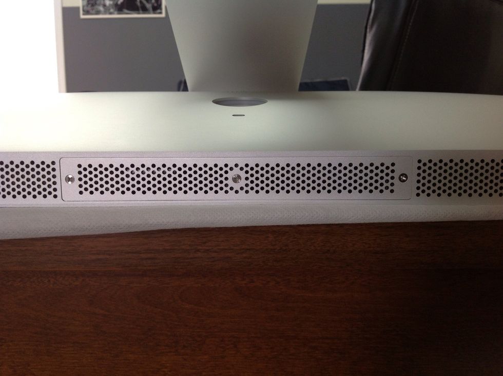 On bottom of screen (under iMac stand) you will find a small cover with 3 Phillips head screws in it.