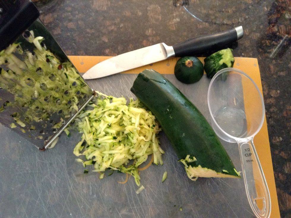 On cutting board, grate 1/2 cup fresh zucchini.