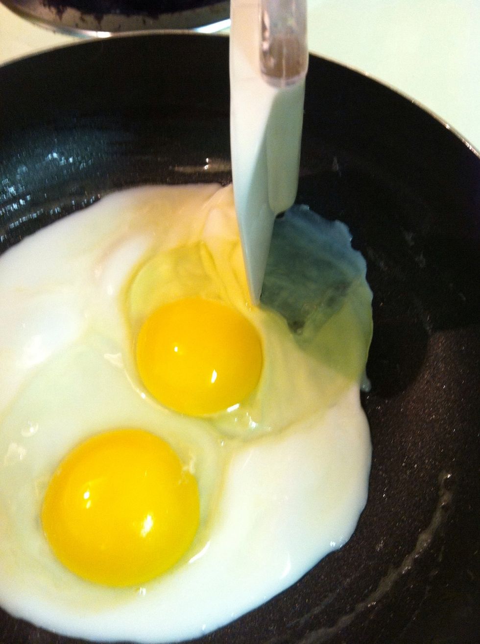 Once it starts becoming solid use your rubber spatula to cut into the center white so it can leak out into the rest of the pan and cook also.