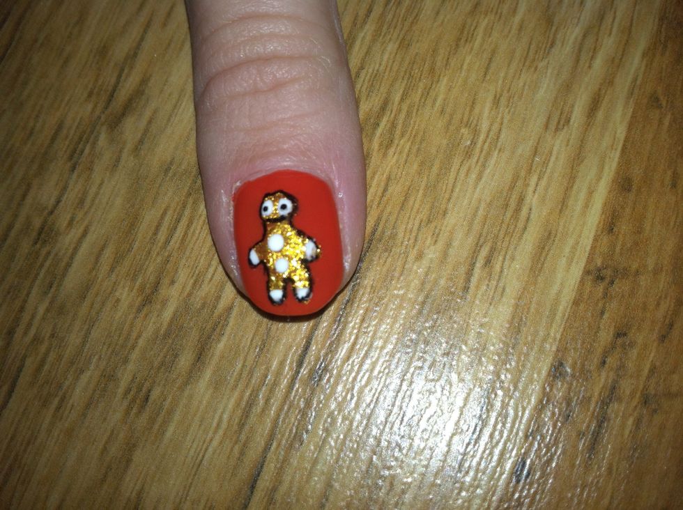 Once the gold shape is dry, bring your gingerman to life by drawing eyes, mouth, buttons and lines on its extremities with white nail polish. I outlined mine with black nail art pen.