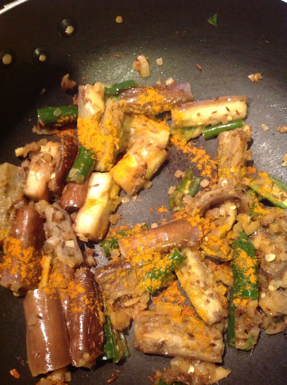Once the onions are cooked, add the eggplant. Add some turmeric and a pinch of red chilly powder.