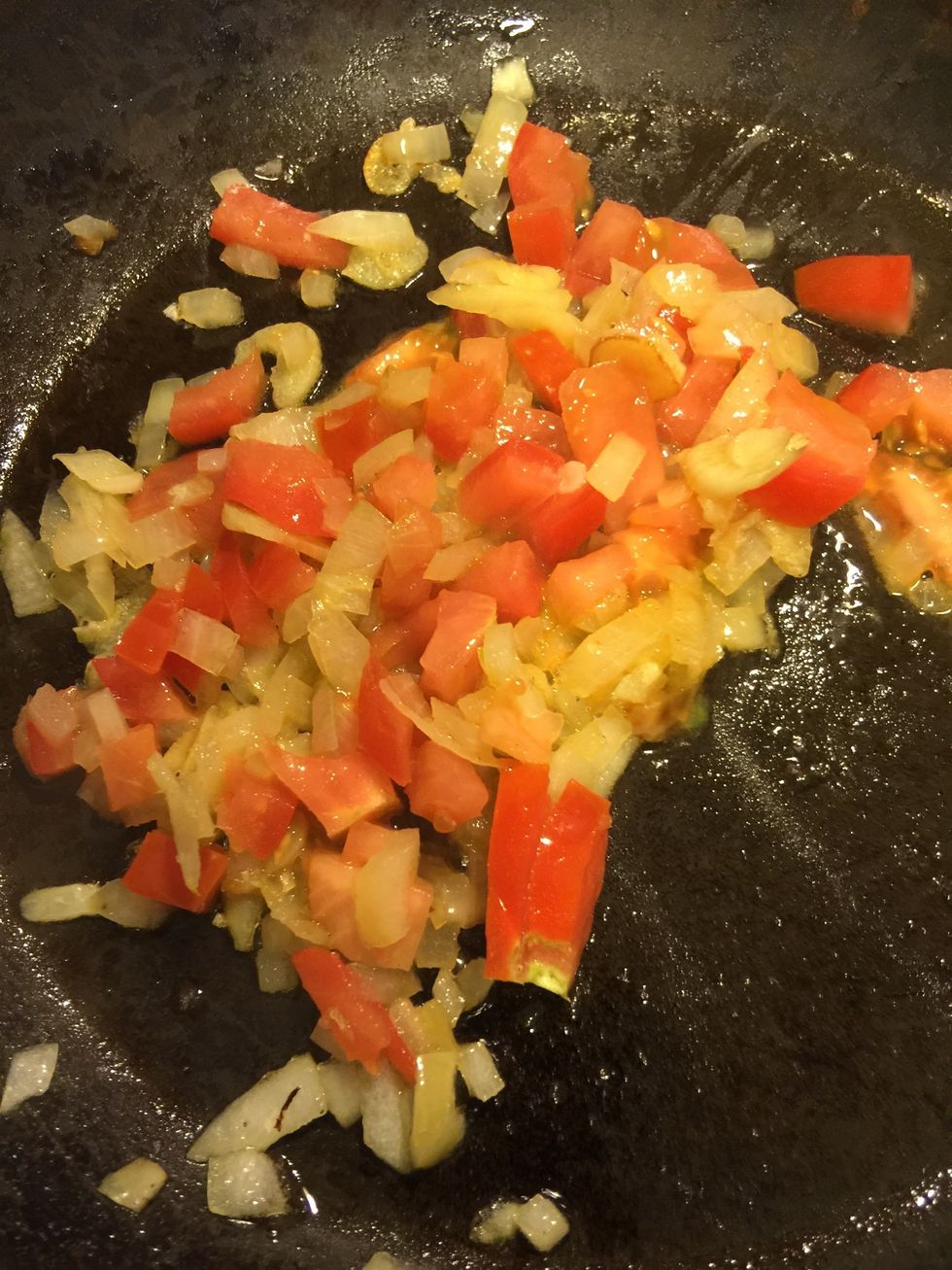 Once the onions start getting pink, add half chopped tomato.