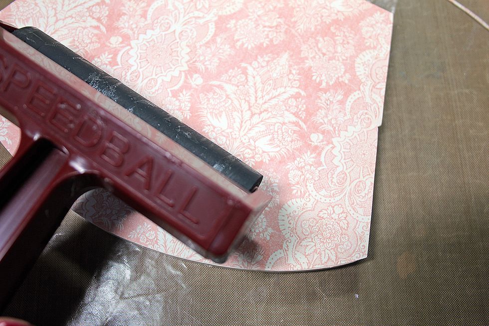 Once the pieces have dried, adhere patterned paper pieces using a quick dry adhesive and a brayer. Using a brayer ensures smooth and even application of the adhesive.