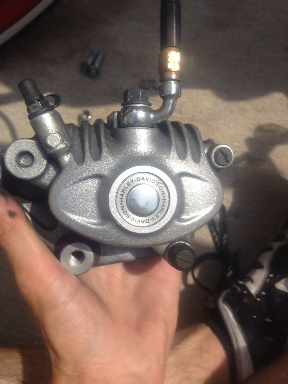 Once the pistons have been depressed and the caliper is off the fork sliders, use the flat head to unscrew the flat head bolt on the upper right hand side.