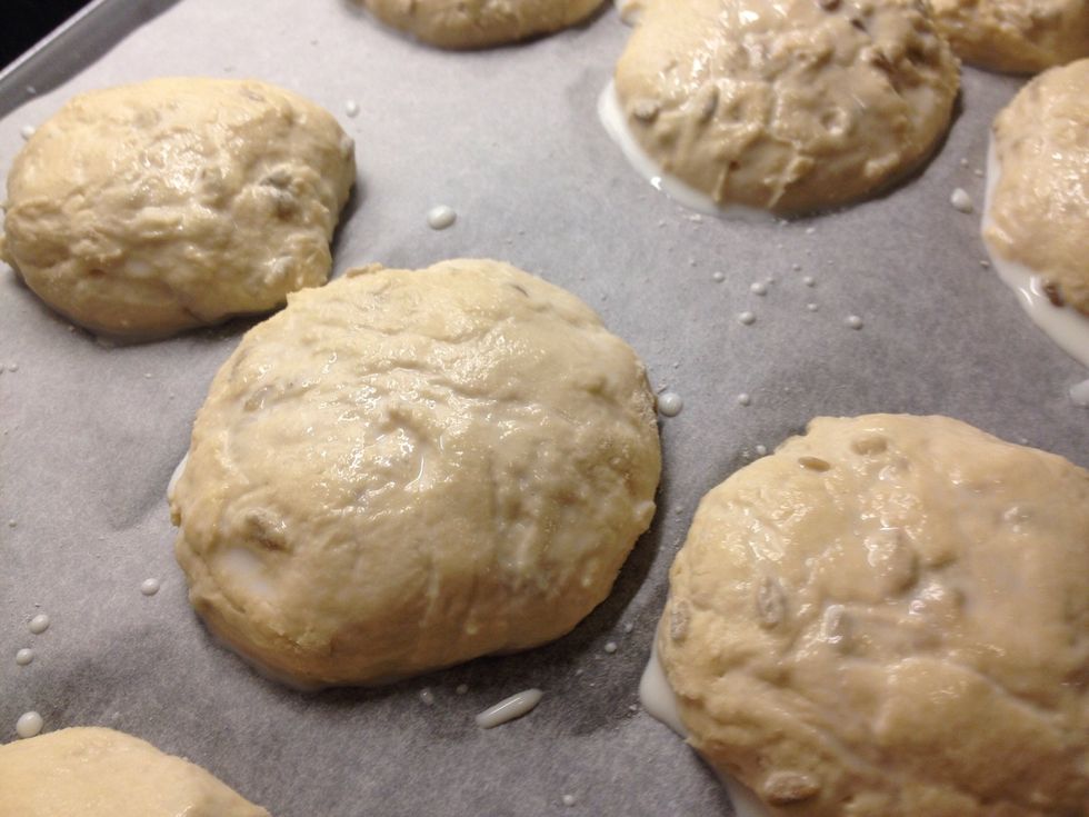 Once they have rested, coat the buns with milk and sunflower seeds.