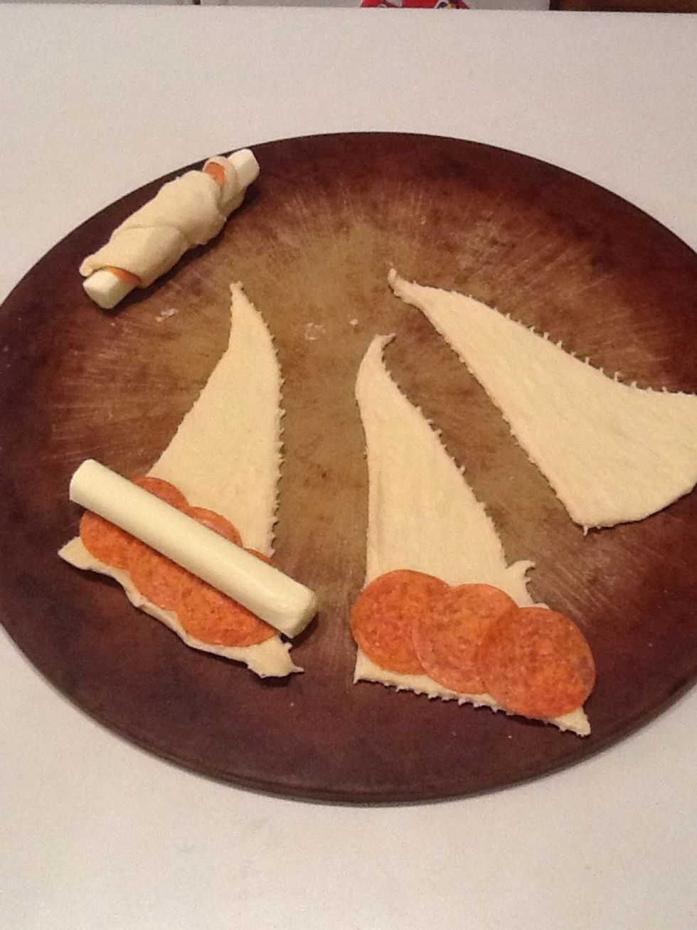 Open container of crescent rolls and unroll each crescent. Lay 3 slices of pepperoni and one string cheese along the largest edge. Roll up and place with end part down.