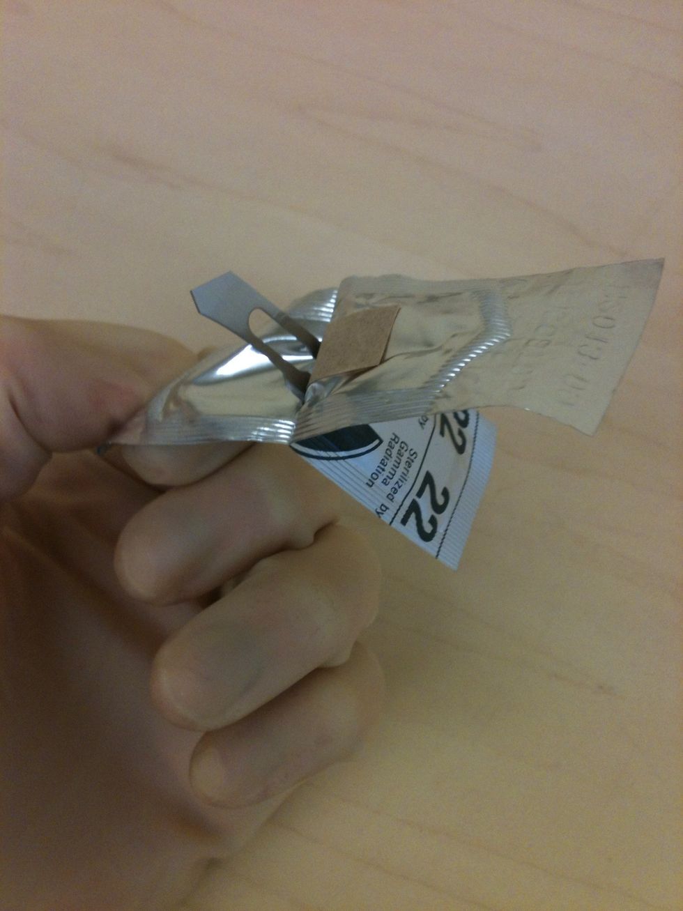 Open the scalpel blade wrapper. Look for the end with a split in the wrapper to ensure you open the dull end.