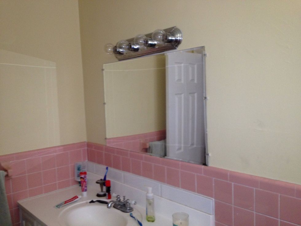 Original Bathroom with ugly mirror, lighting, pale yellow paint and pink tiles.