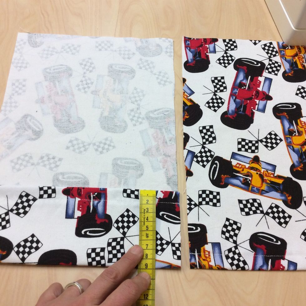 P\u00e5 den l\u00e4ngre av bitarna m\u00e4ter du nu och viker in 9 cm mot avigsidan av tyget. S\u00e4tt fast med n\u00e5gra n\u00e5lar.