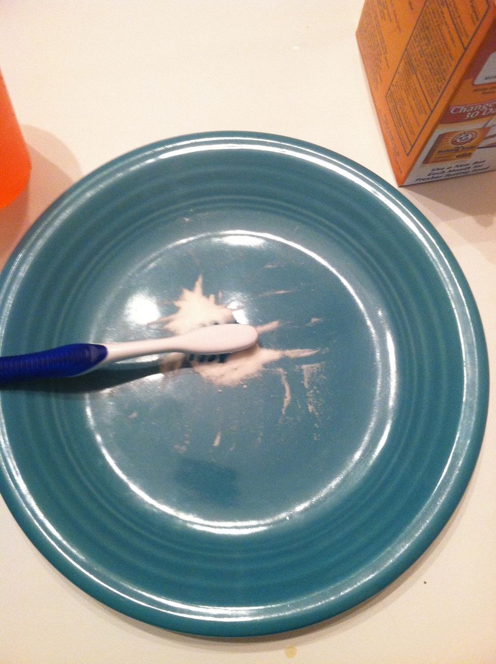Pack baking soda on toothbrush, by pressing toothbrush into plate.