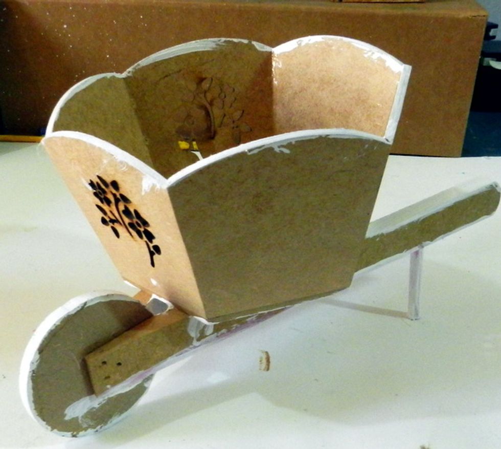 Paint the edges of the wooden wheelbarrow using acrylic gesso.