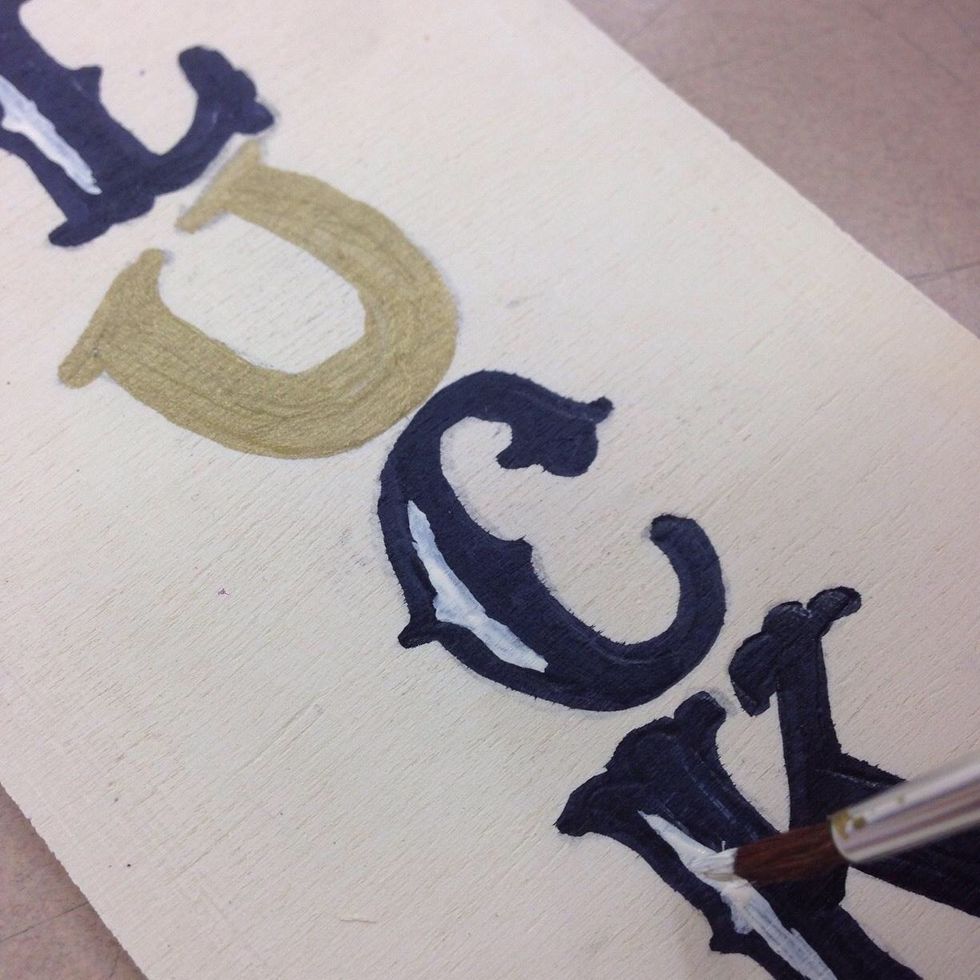 Paint the 'U' with metallic gold paint and add the letter highlights with light ivory. You may need to add another coat of light ivory for good coverage.