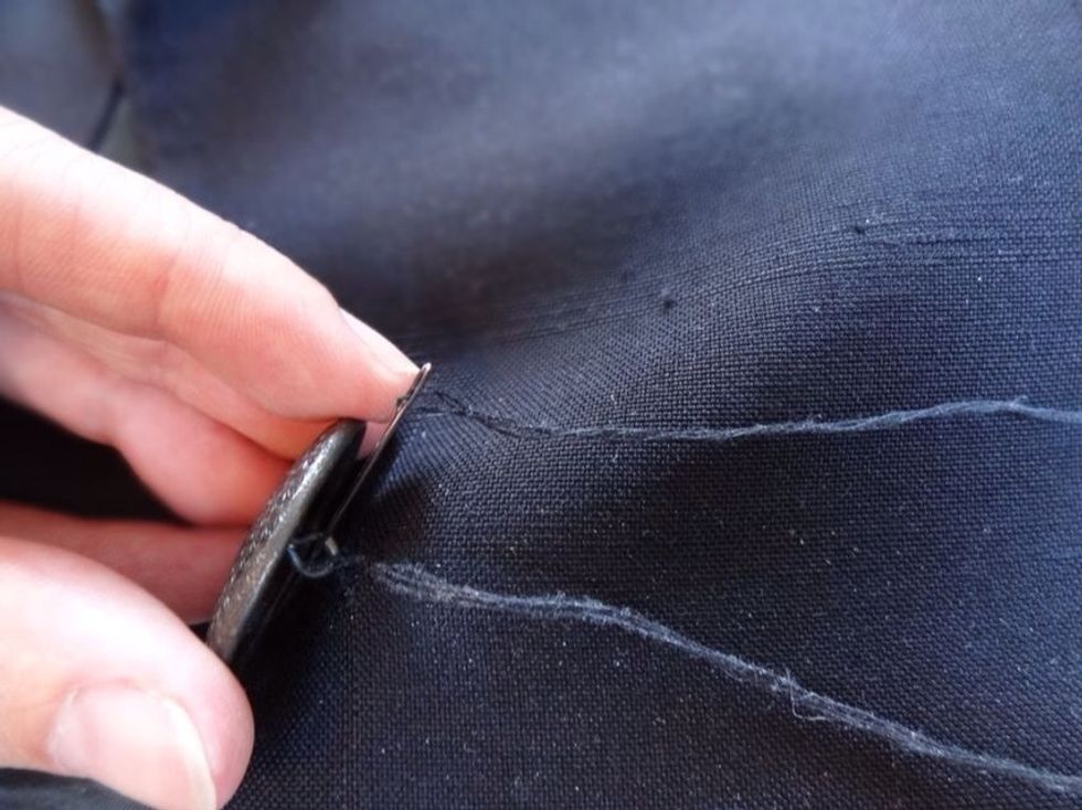 Pass the thread into the fabric of the top side of the coat and up again through the round hook of the button. Continue looping several times until the button is secure.
