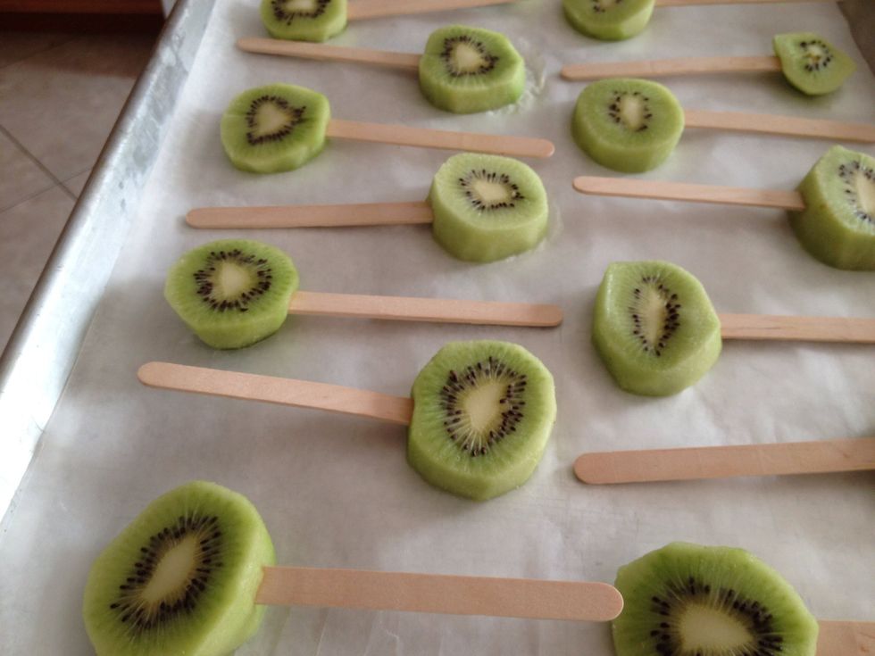 Peel and cut your kiwis. Stick a popsicle stick in each slice, and freeze in the freezer for 15 minutes on a lined baking sheet.