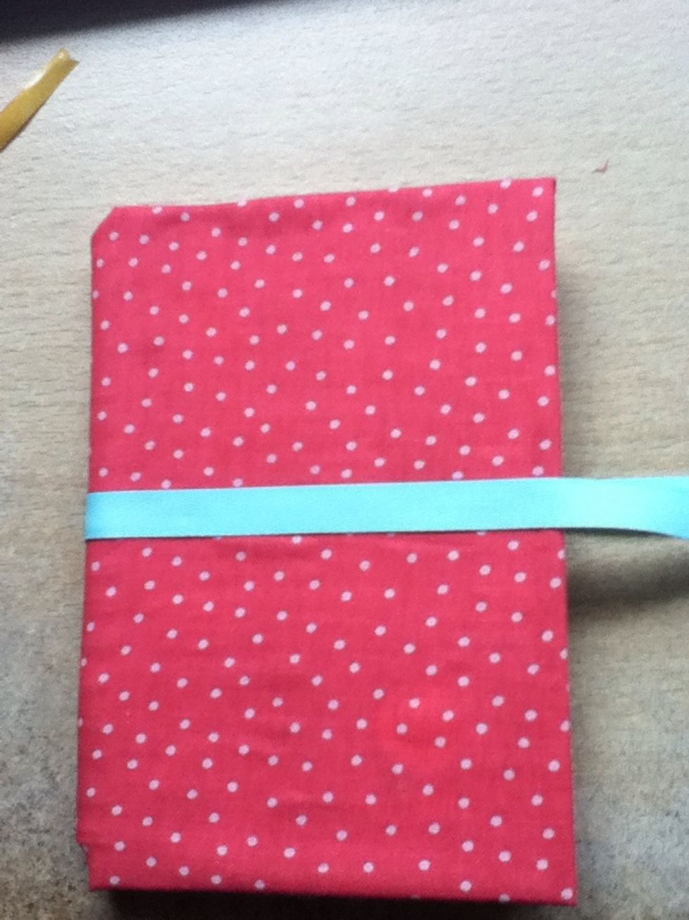 Peel off the top layer of tape, and wrap a ribbon around the book. This ribbon needs to be quite long; you'll see why in the next step.
