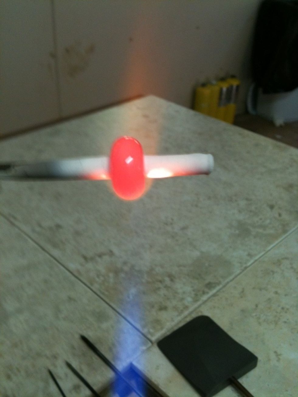 Photographing a spinning molten glass thru safety glasses is tough! This is the core layer of hot black glass being worked onto the coated mandrel in the torch's flame.