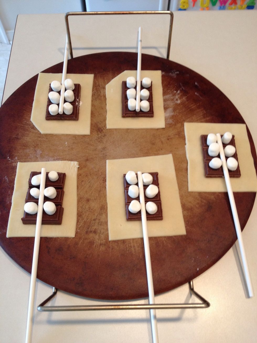 Place 6 marshmallows on each piece of chocolate and place the stick in the middle.   It's OK if the stick won't lay flat.  You can make it more stable when you add the top in a few minutes.