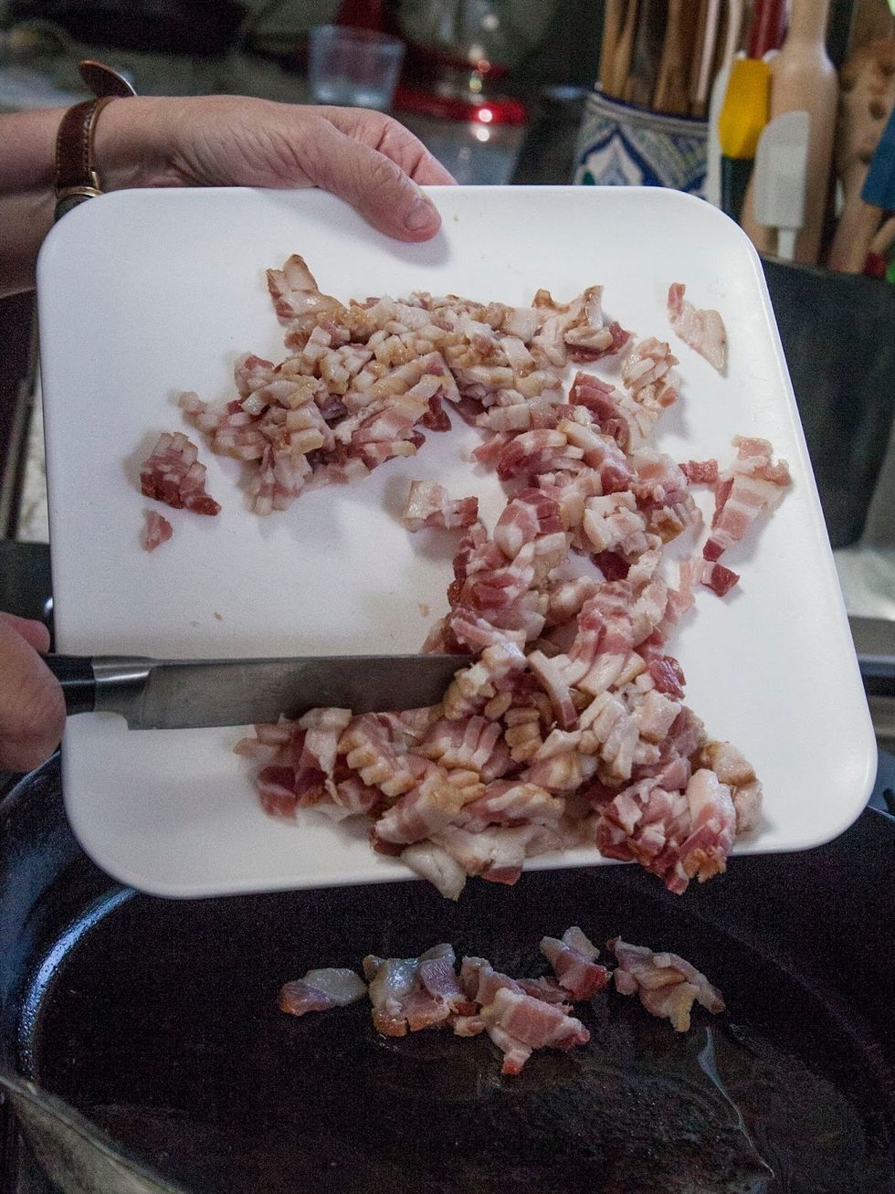 Place a cast iron pan on the fire. When it's hot, add in the chopped bacon.