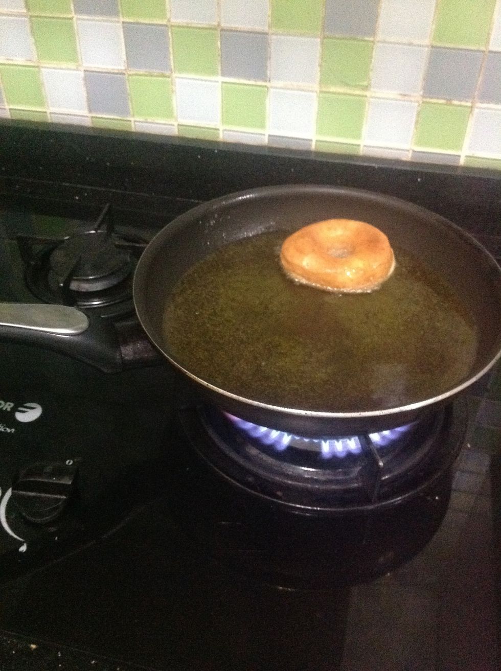 Place a doughnut into the hot oil and cook it for about 2 minutes on each side or until golden brown.
