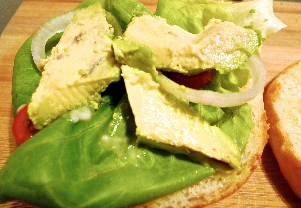 Place a lettuce leaf, onion rings, avocado and cherry tomatoes on the upper half of the bun.