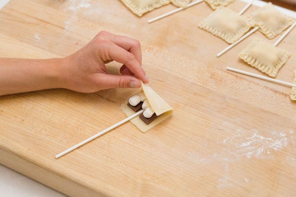 Place a lollipop stick between the two chocolate pieces about halfway down the crust rectangle and press down lightly. Then, fold over the other half of your crust piece. 