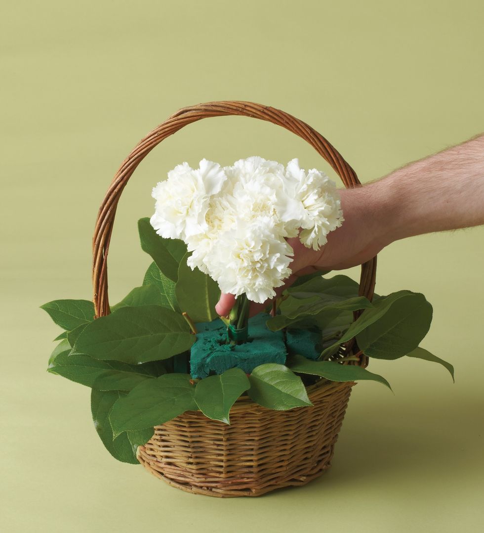 Place block of floral foam in a basket with liner and layer the salal on bottom, surrounding foam and place the carnations stems of the puppy's head in the floral foam