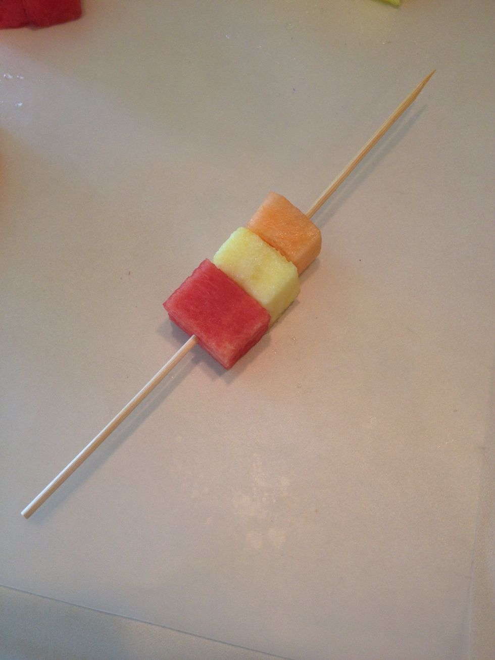 Place one watermelon, cantaloupe, and pineapple cube on wooden skewer.