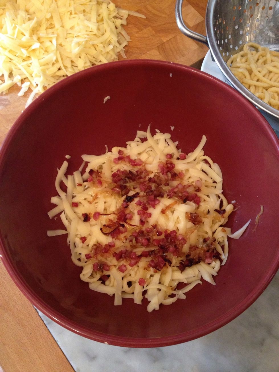 place sp\u00e4tzle in bowl and add a layer of cheese, then some bacon and onions