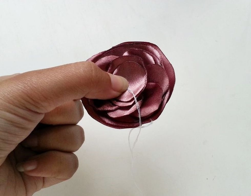 Place the 2 base pieces under the stitched piece. And then place the 2 center pieces on their position. Prepare needle and thread and draw it through the center of the satin layers.