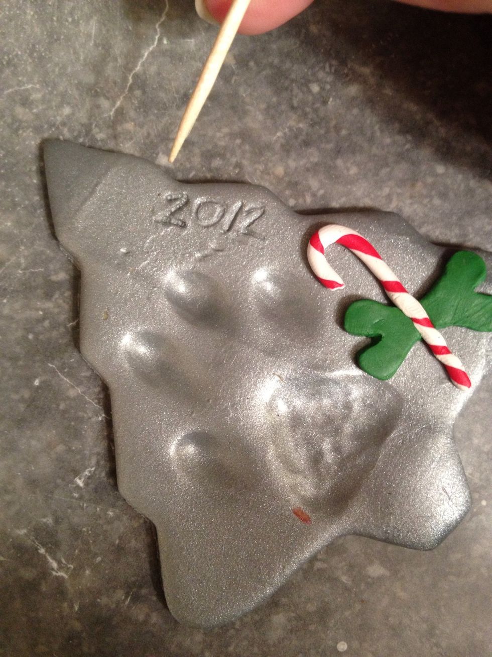 Place the bone under the cane, and put the cane into the dent you made in the center of the bone. Push down slightly to adhere the two together onto the ornament. Write the year using a toothpick.