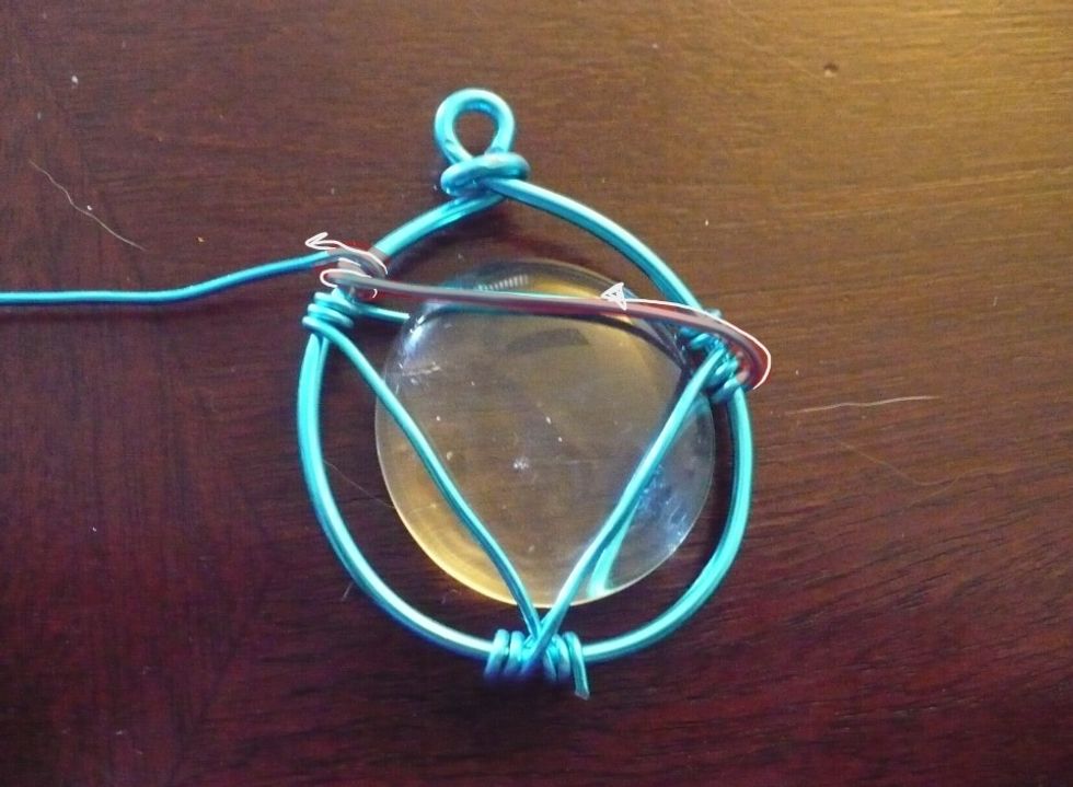 Place the gem into the wires between the top and bottom layers. It should slide right in. Pull the thin wire over the gem to the top left. Wrap twice!