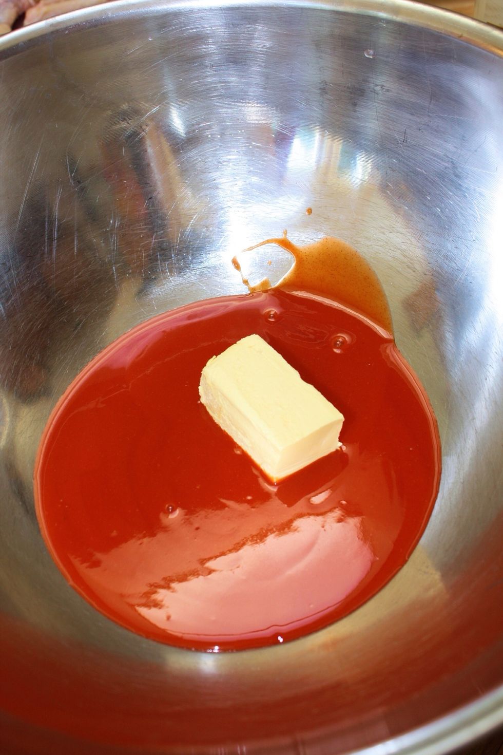 Place the sauce with several pats of butter in a large kitchen mixing bowl. Amounts of each will depend on how big a batch of wings you're planning to make.