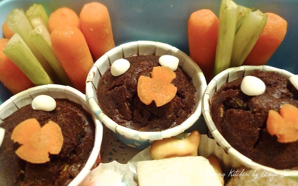 Place the zucchini muffins in the upper half of a lunchbox. Decorate with white chocolate chips and carrot florets. Also add baby carrots and celery for extra veggie servings and colours.