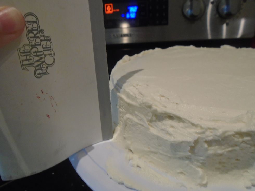 Place your bench scrapper up against the frosting. Hold it there firmly. Turn the turn table making sure to press the bench scrapper against the frosting.