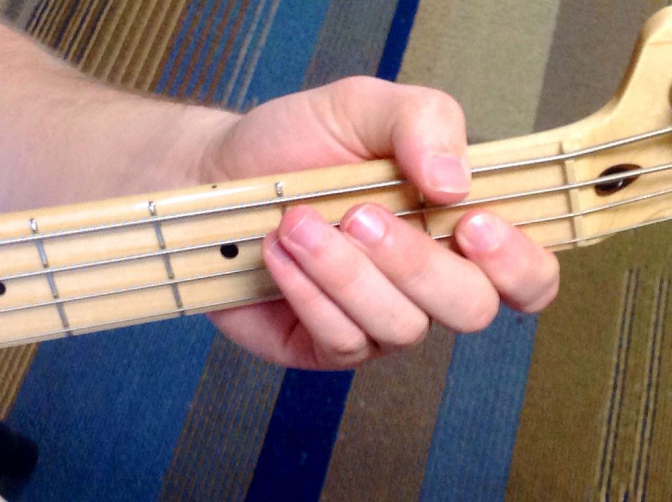 Place your finger between the nut and first fret on the D string. This is the fourth note in the scale, E flat.