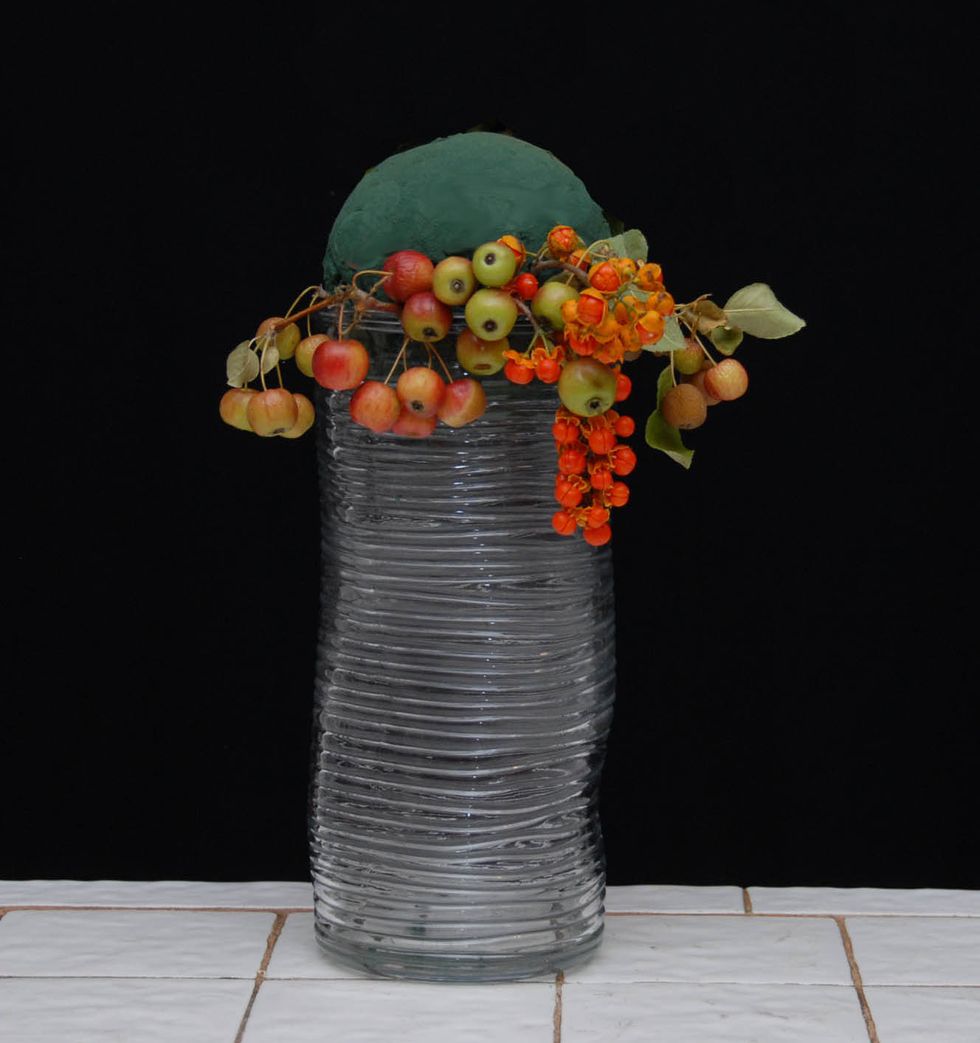 Placing a sphere of foam solidly onto the top of a container as shown. Place berry type/sized material, such as  bittersweet, or malus, etc. around the lower section of the sphere.