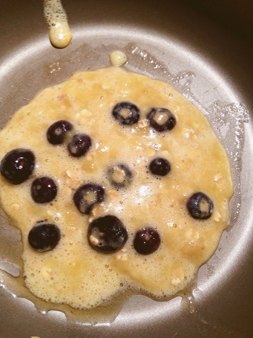 Pour in the batter with some blueberries. It's okay if the pancake is a little uneven, it'll still taste awesome!