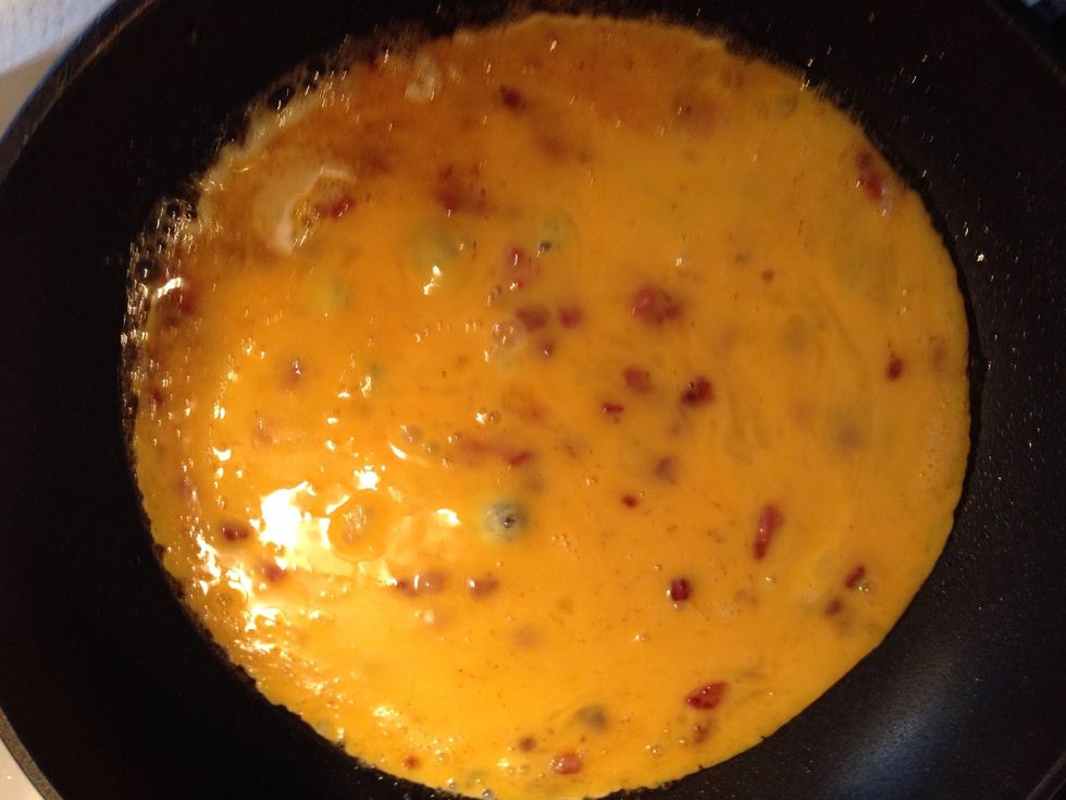 Pour in the whisked eggs with sliced bacon. After a few moments lift the rim with a spatula and let the liquid egg flow underneath. That way your omelette will fry more evenly.